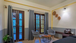 A hotel room with a bed, two chairs, a small table, a potted plant, and a window with curtains. - The Hosteller Coorg Rainforest, Madikeri (Madikeri)