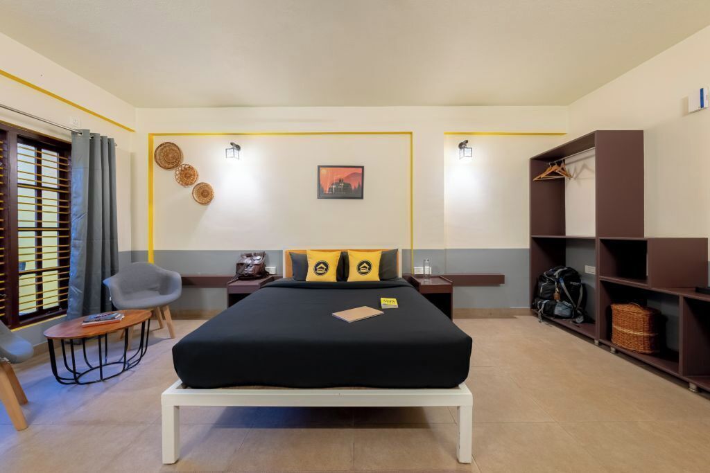A hotel room with a bed, a chair, a small table, a wardrobe, and a window with curtains.