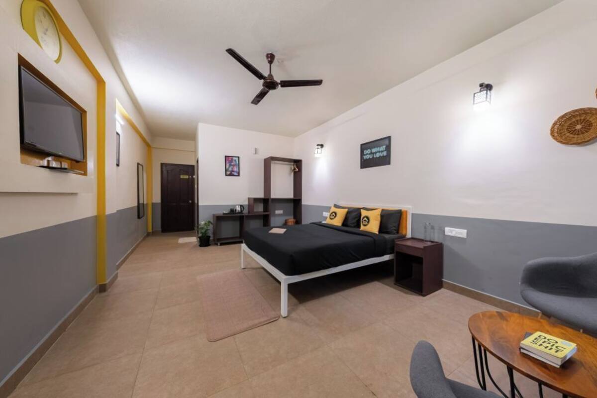 A hotel room with a bed, a desk, a chair, a TV, and a ceiling fan.