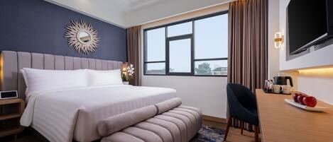 Habitación de hotel moderna con una cama grande, un escritorio con silla, un televisor de pantalla plana y una ventana con cortinas.