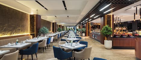 A modern restaurant with long tables, blue chairs, and a central buffet area.