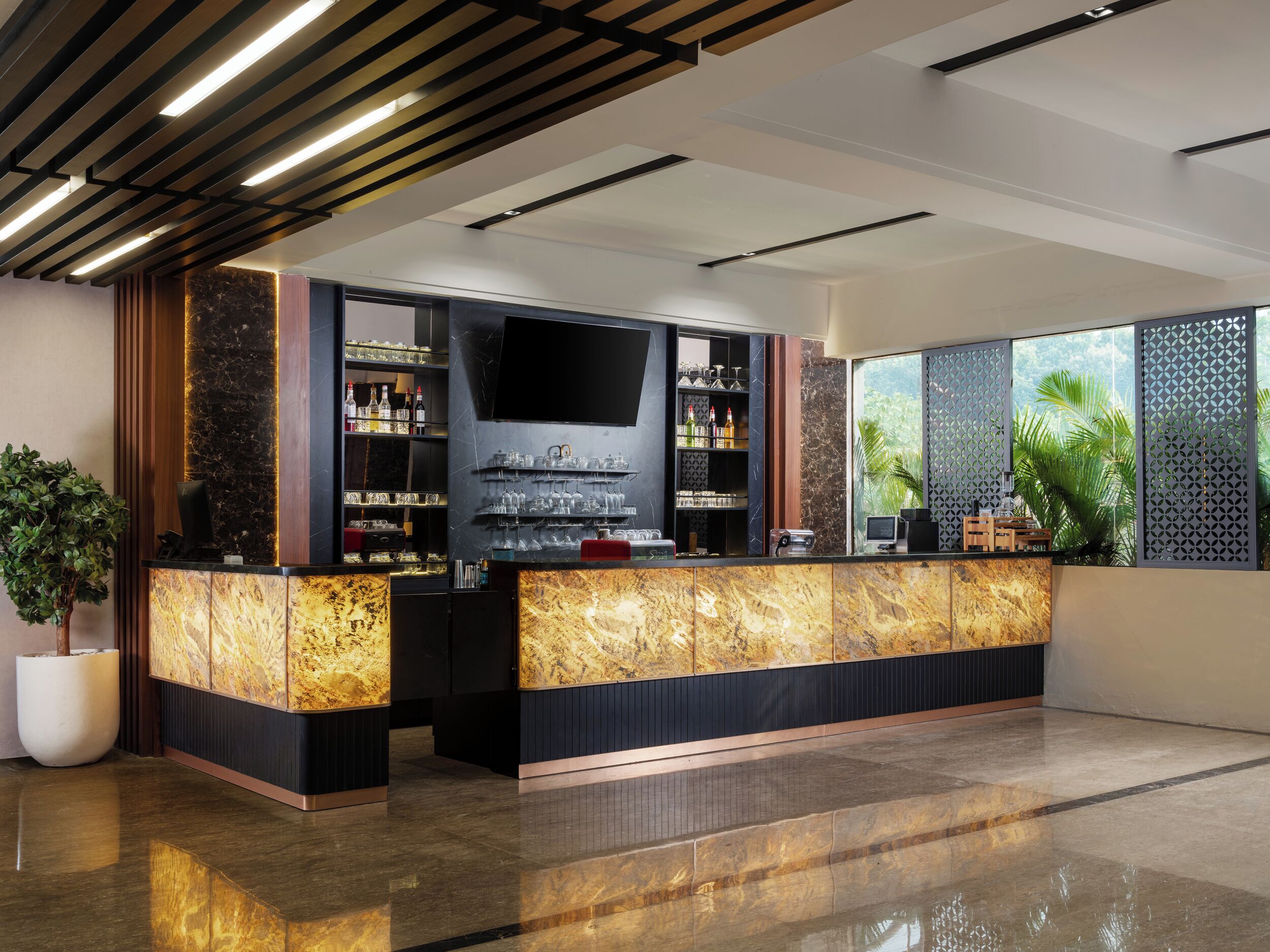 A modern bar area with a marble countertop, shelves with bottles, and a large TV screen.