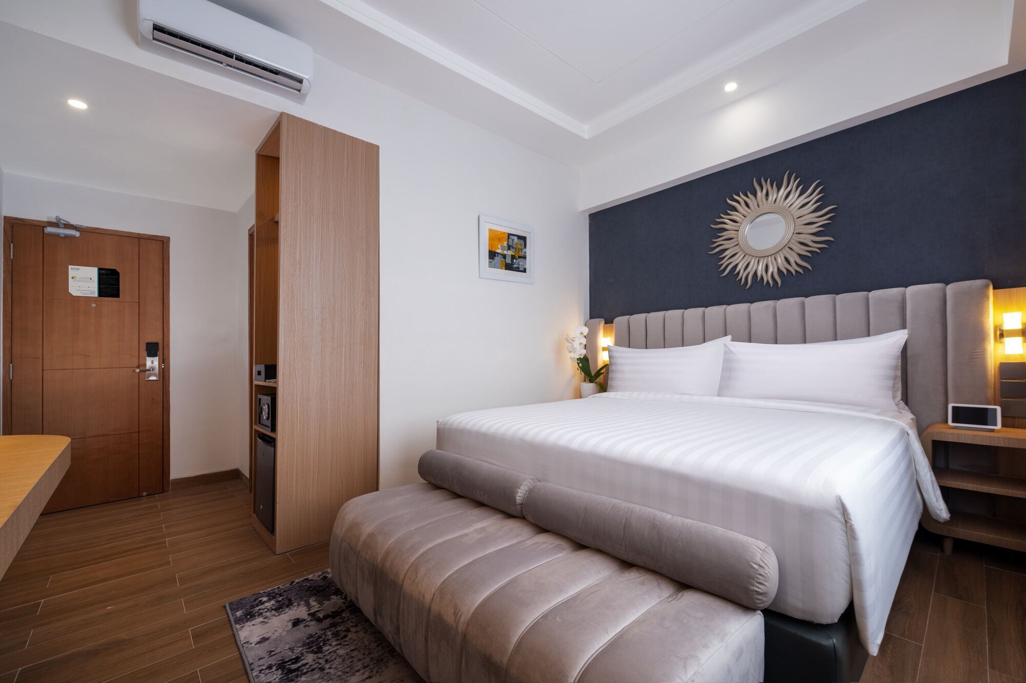 Habitació d'hotel moderna amb un llit gran, una banca, un escriptori i un armari.