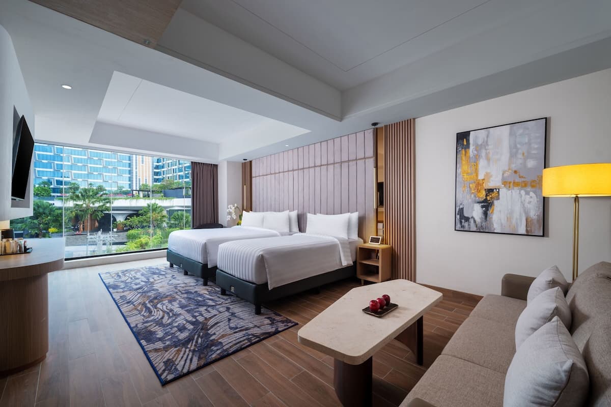 A modern hotel room with a large bed, a desk, a sofa, and a view of the cityscape.