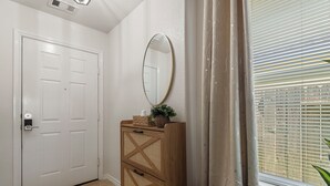 A hallway with a white door, a wooden cabinet with a mirror, and a window with blinds. - Relax, Quiet, Clean, & 15min Away From Airport (Houston)