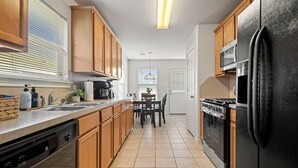 A modern kitchen with wooden cabinets, a black refrigerator, stainless steel appliances, and a dining area with a table and chairs. - Relax, Quiet, Clean, & 15min Away From Airport (Houston)