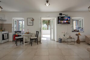 A modern living room with a dining area, a TV mounted on the wall, and a view through an open door.