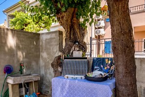 A tree with a table underneath, a concrete wall, and a building with air conditioning units in the background. - Harmony House Vito With Lovely Terrace, Lopar, Croatia (Lopar)