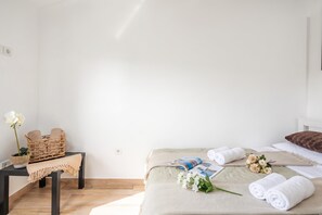 Une chambre d’hôtel propre et minimaliste, avec un lit, une petite table agrémentée d’un panier et de fleurs, et une table de chevet sur laquelle se trouvent un magazine et des serviettes.