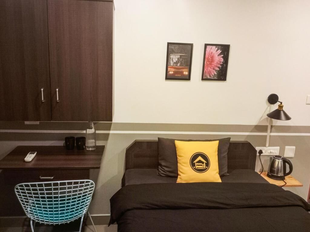 Un dormitorio con cama, escritorio, silla, lámpara y estante en la pared.