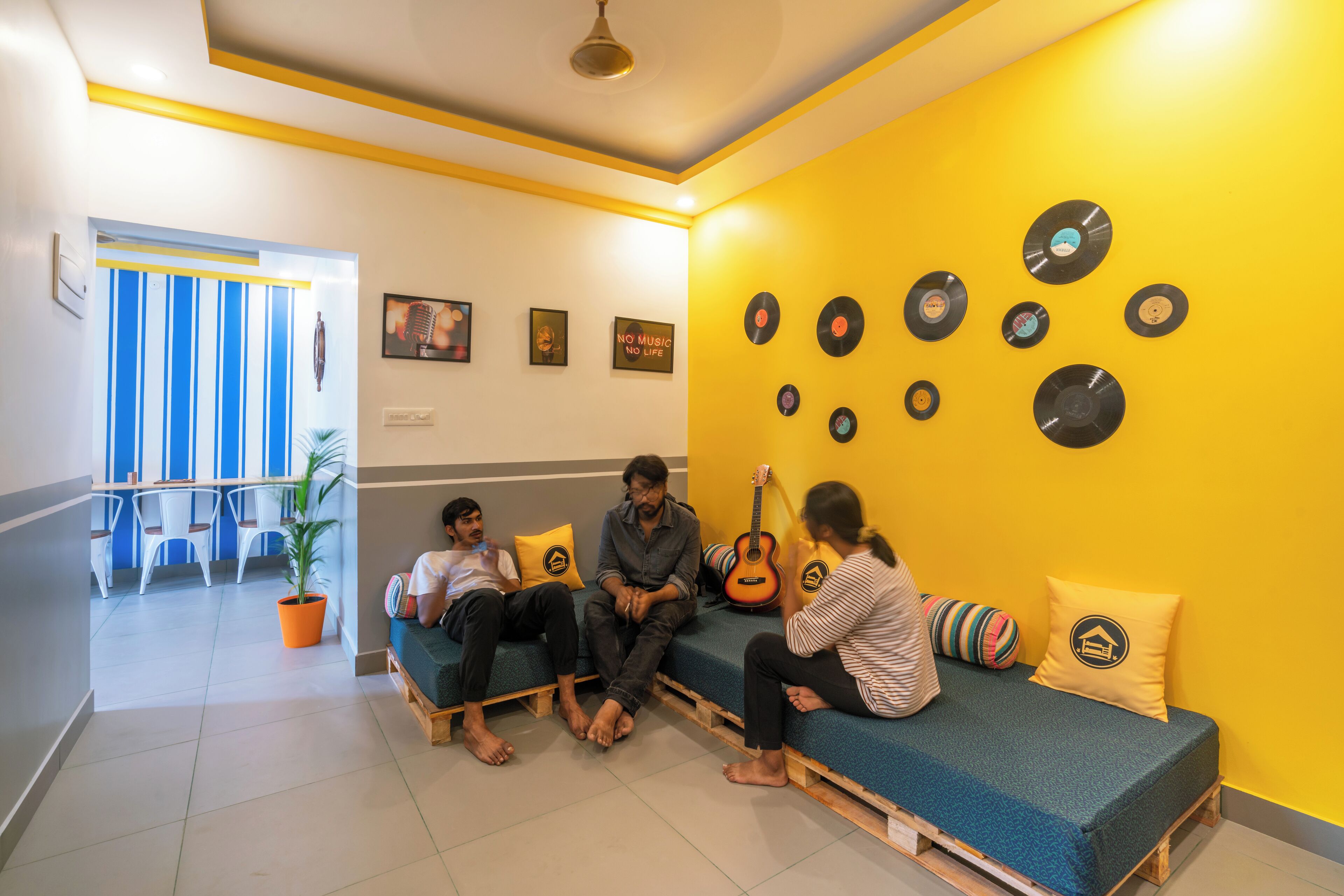 A room with a yellow wall, a guitar, and a group of people sitting on a bench.