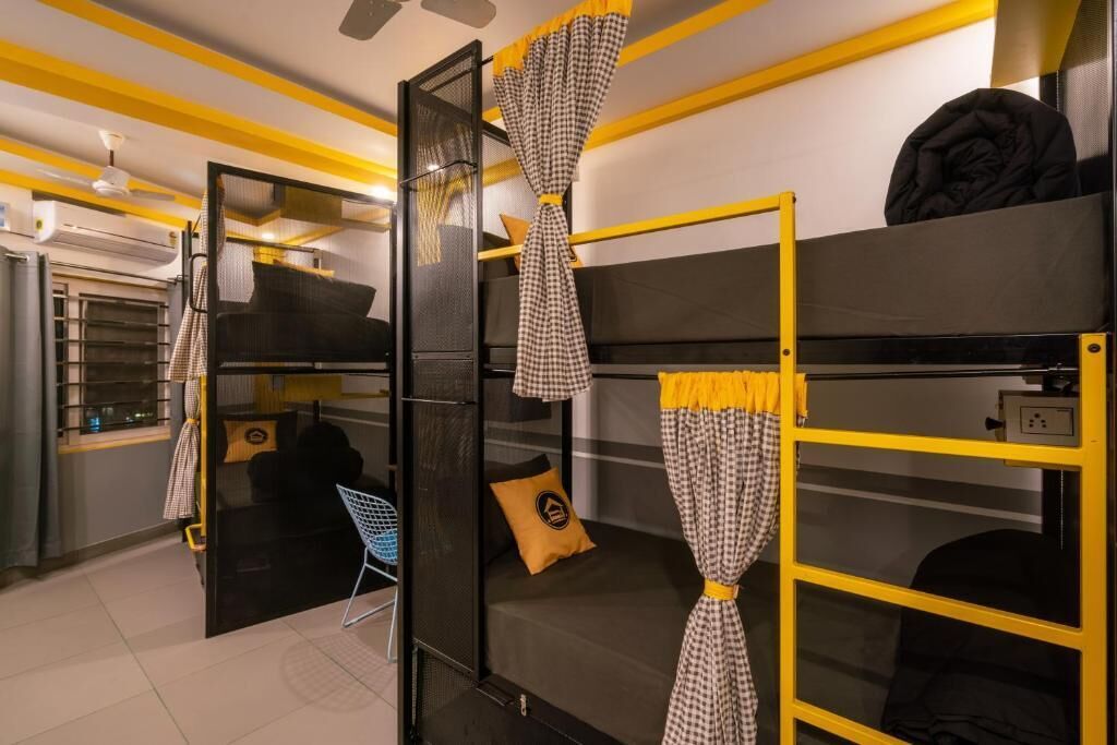 A compact hotel room with bunk beds, a small kitchenette, and a mirror with curtains.