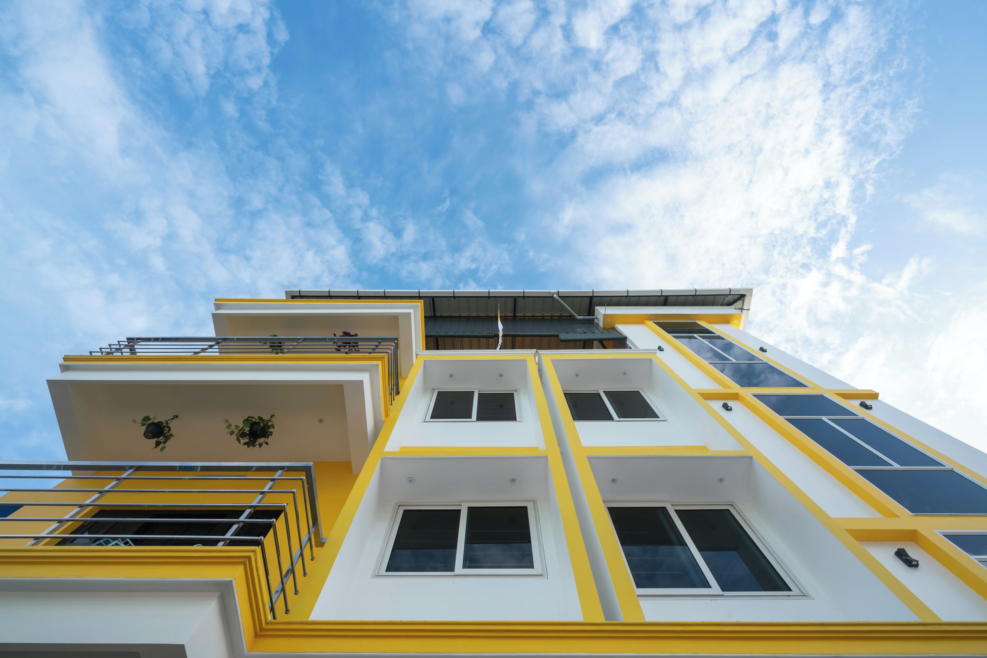Un edificio de varios pisos con fachada amarilla y blanca, varios balcones y ventanas amplias.