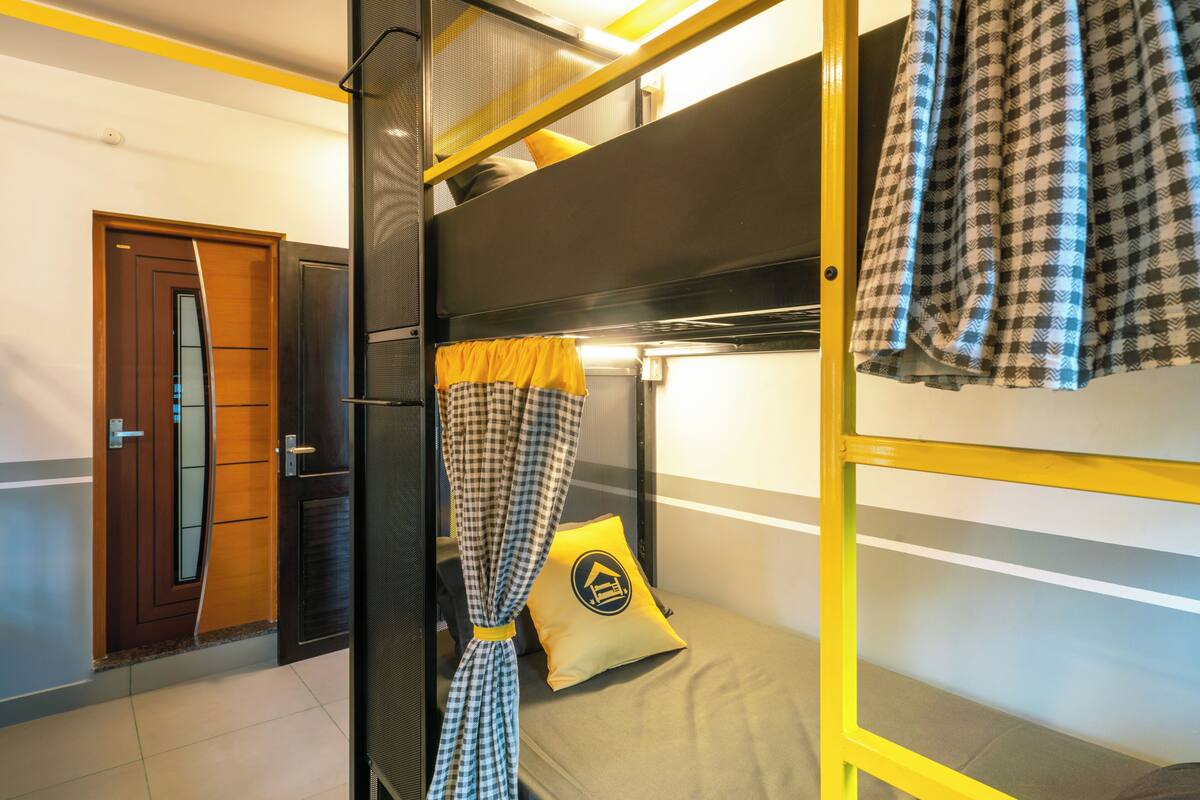 A bunk bed room with a checkered curtain, a yellow pillow with a house logo, and a wooden door.