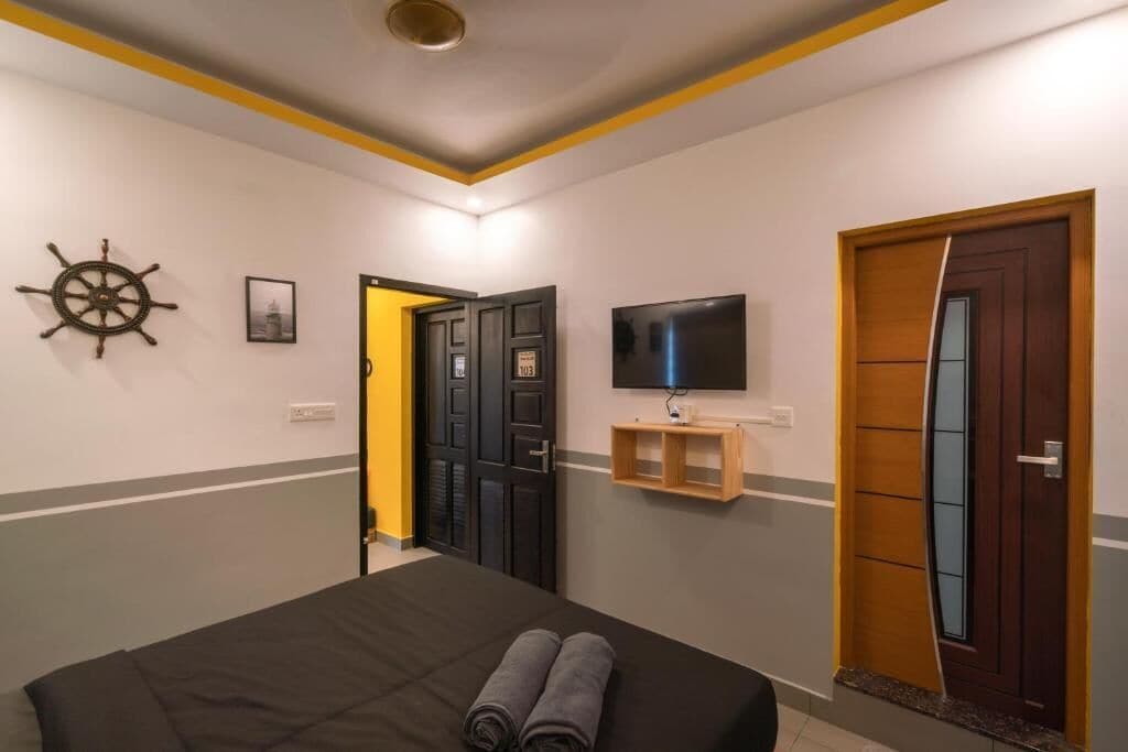 A hotel room with a bed, a TV mounted on the wall, a wooden door, and a wall-mounted shelf.