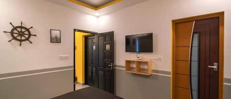 Habitación de hotel con cama, televisor montado en la pared, puerta de madera y repisa en la pared.