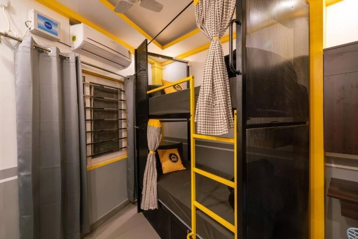 A compact room with bunk beds, a window with bars, an air conditioning unit, and a checkered curtain.