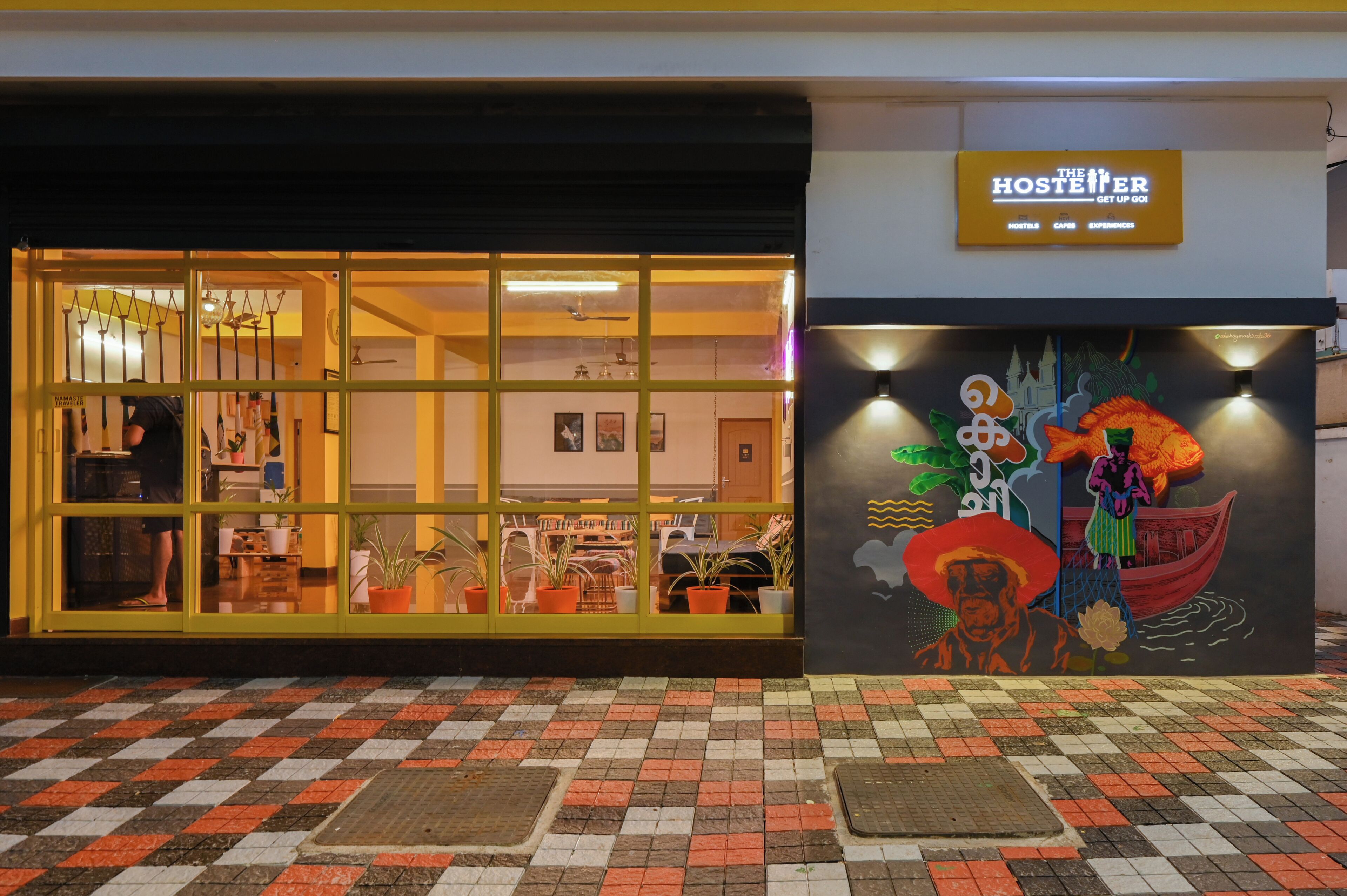 A hostel with a large window display, a sign reading "The Hosteler," and a colorful mural on the wall.