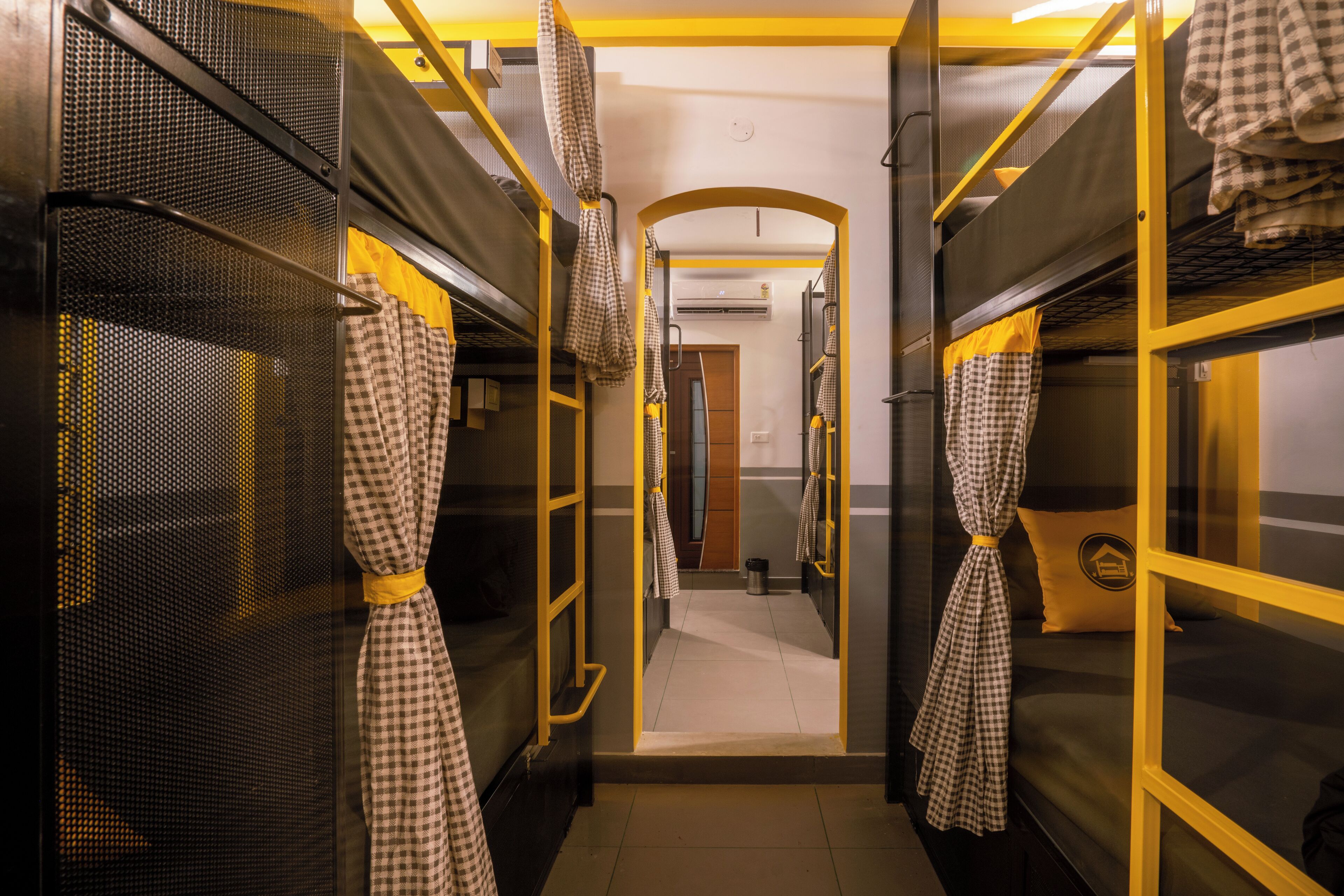 A corridor with bunk beds, checkered curtains, and a yellow railing.