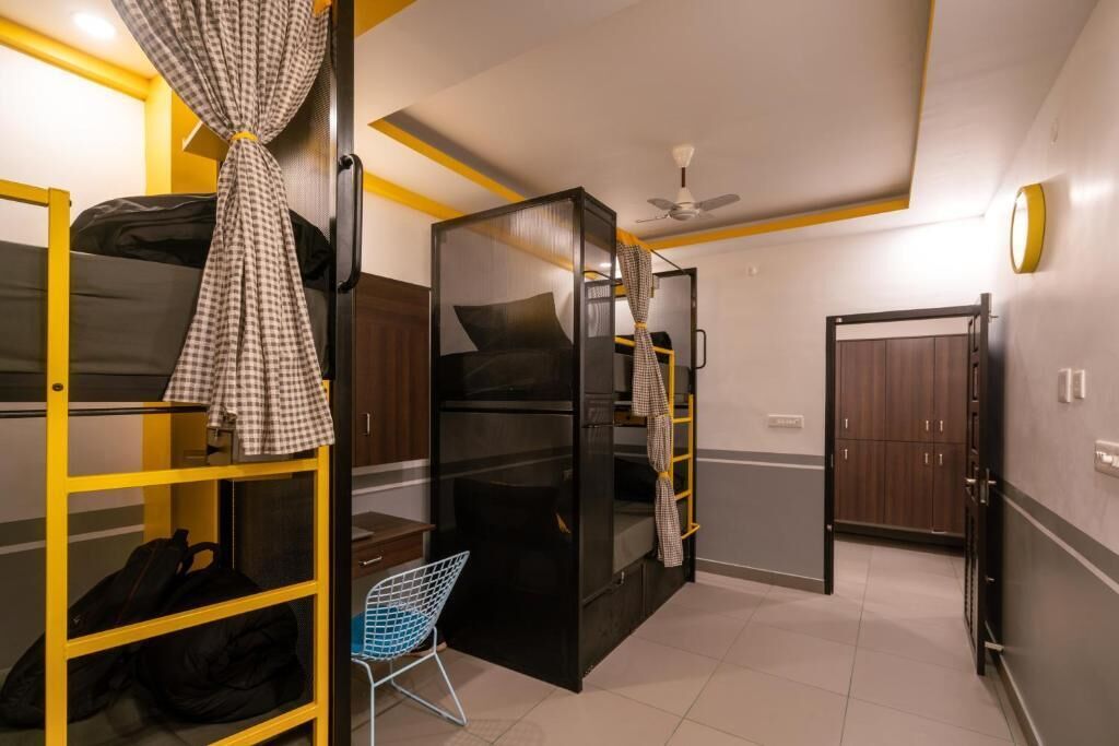 A compact hotel room with a bunk bed, a small seating area, a wardrobe, and a ceiling fan.