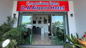 The exterior of D.A Airport Hotel with a red sign, glass doors, and a welcome mat.