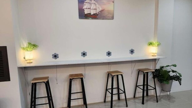A bar area with four stools, a wall-mounted shelf with decorative items, and a potted plant. - DA Airport Hotel (Sa Khu)