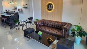 A modern living area with a leather sofa, a glass coffee table, and a bar area with a wooden accent wall and a logo.