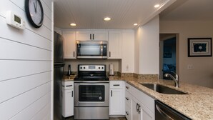 Una cocina moderna con armarios blancos, estufa de acero inoxidable, microondas y encimera de granito.