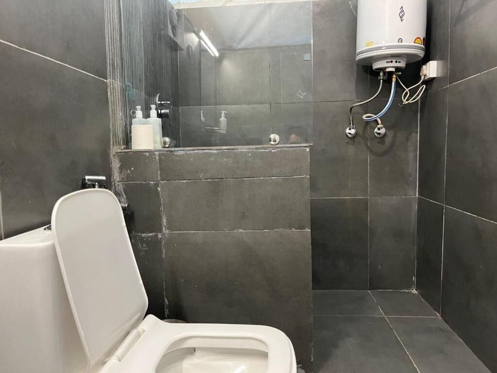 A small, modern bathroom with a white toilet, a shower area, and a water heater mounted on the wall.