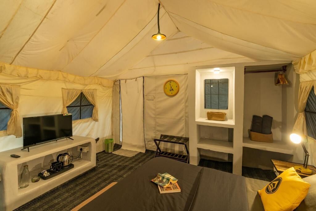 Habitación tipo tienda de campaña con una cama, un televisor, un reloj y estantes con objetos personales.