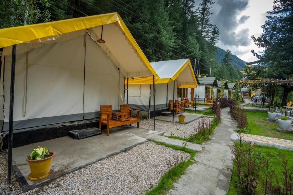 A row of tents with wooden furniture and a gravel path.