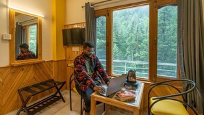 Ein Zimmer mit großem Fenster, einer hölzernen Bank, einem Tisch mit Laptop und einem Stuhl.