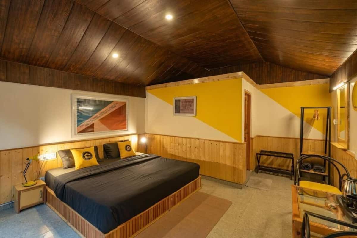 Une chambre avec un plafond en bois, un lit avec un matelas noir, une table de chevet en bois, une chaise et un miroir.