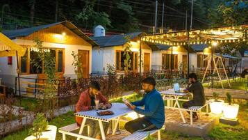 Guests can enjoy meals and conversation in this serene outdoor seating area surrounded by lush greenery and string lights.