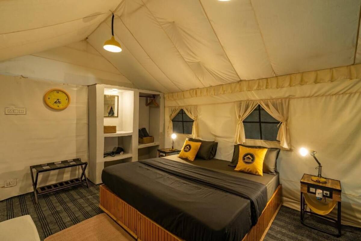 Une pièce aménagée avec une tente, un lit, une table de chevet, une lampe et une horloge au mur.