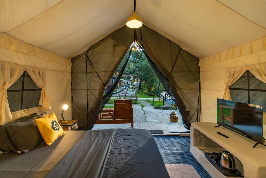 A tented accommodation room with a bed, a television, and a view of the outdoors.
