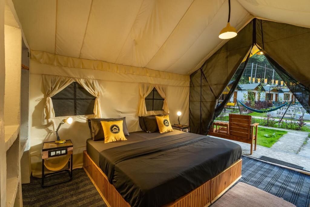 Un dormitorio tipo tienda de campaña con cama, mesitas de noche y vistas al exterior.