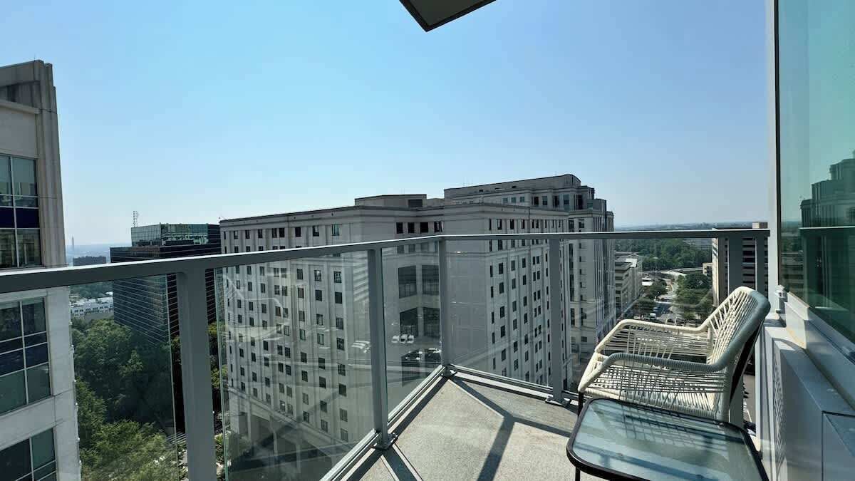 A high-rise building with a glass balcony, offering a view of other buildings and a distant cityscape.