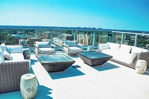 A rooftop terrace with outdoor furniture, a glass balustrade, and a cityscape view.