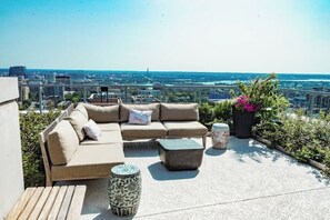 A rooftop terrace with a beige sofa, two side tables, and a potted plant.