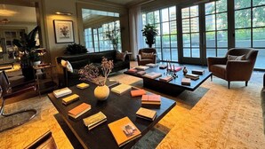 Een ruime lobby met een bank, fauteuils, een bijzettafeltje met boeken en grote ramen met uitzicht op de omgeving.