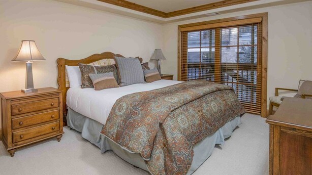 A bedroom with a wooden bed, a nightstand, a dresser, and a window with blinds. - Luxury 4 Bedroom Condo in Vail Village - Mountain View Residences (Vail)