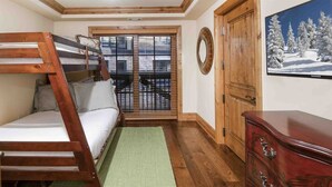 Ein Zimmer mit Etagenbett, einem hölzernen Schminktisch, einem grünen Teppich und einem Fenster mit Jalousien.