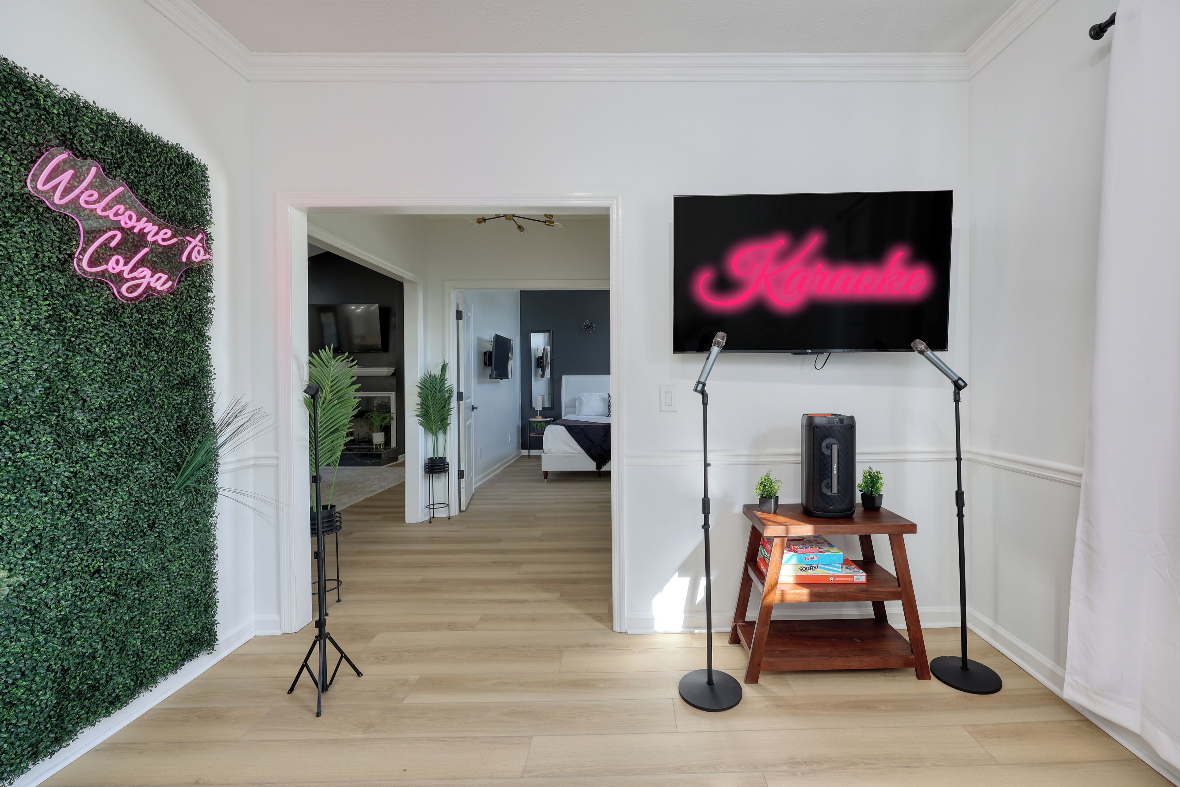 Een moderne woonkamer met een groene wand, een neonbord, een wandgemonteerde televisie en een houten bijzettafeltje met een speaker.