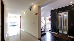 A hotel corridor with a shiny tiled floor, a staircase with a metal railing, and a glass elevator. - Laxmi Mahal (New Delhi)