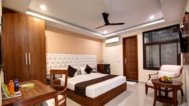 A modern hotel room with a large bed, a dining table, a TV, and a ceiling fan. - Laxmi Mahal (New Delhi)