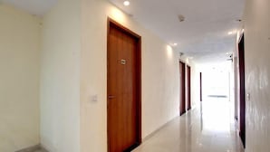 A corridor with a wooden door, a light switch, and a tiled floor. - Laxmi Mahal (New Delhi)