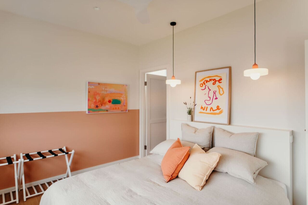 Une chambre à coucher avec un lit, deux lampes suspendues, un tableau encadré et une petite table avec une chaise.