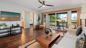 A spacious living room with a large flat-screen TV, wooden coffee table, and a ceiling fan. - 2BD Pool & Resort's Amenities, Ocean Views! - Kaanapali Plantation 34 (Lahaina)