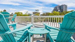 Eine Terrasse mit türkisfarbenen Adirondack-Stühlen und einem kleinen Tisch, mit Blick auf einen Strand und Gebäude.